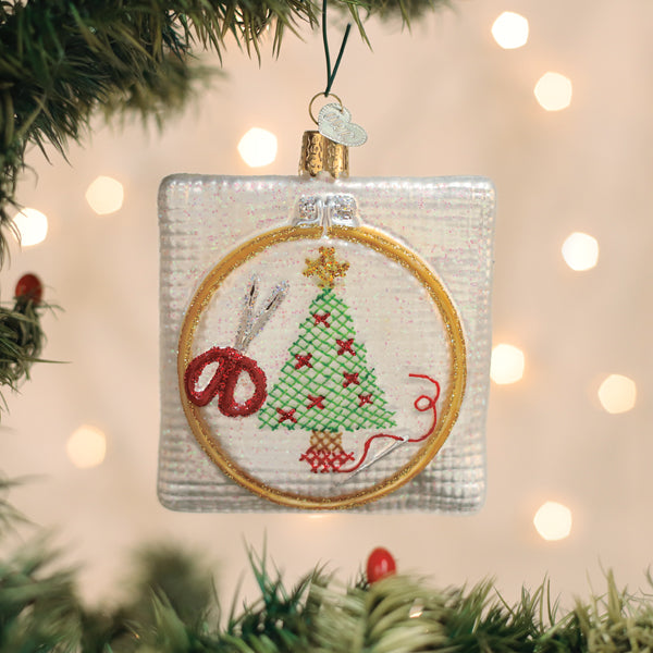 Decorative Christmas ornament with embroidery hoop and cross-stitched tree design, hanging on a Christmas tree.