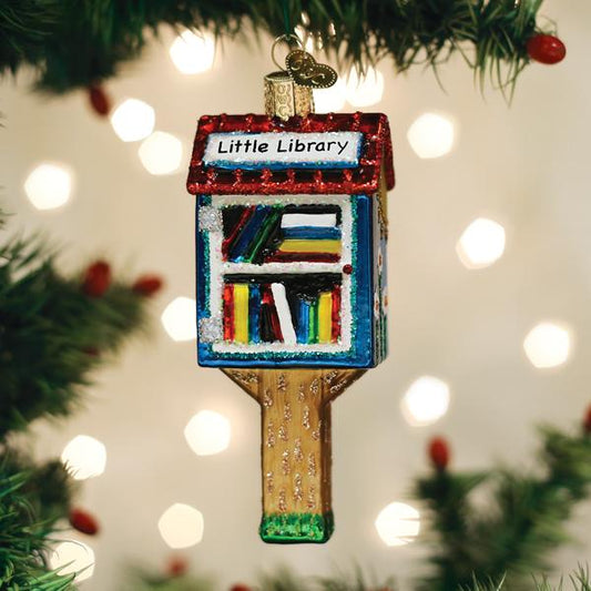 Decorative ornament shaped like a 'Little Library' on a Christmas tree with blurred lights in the background.
