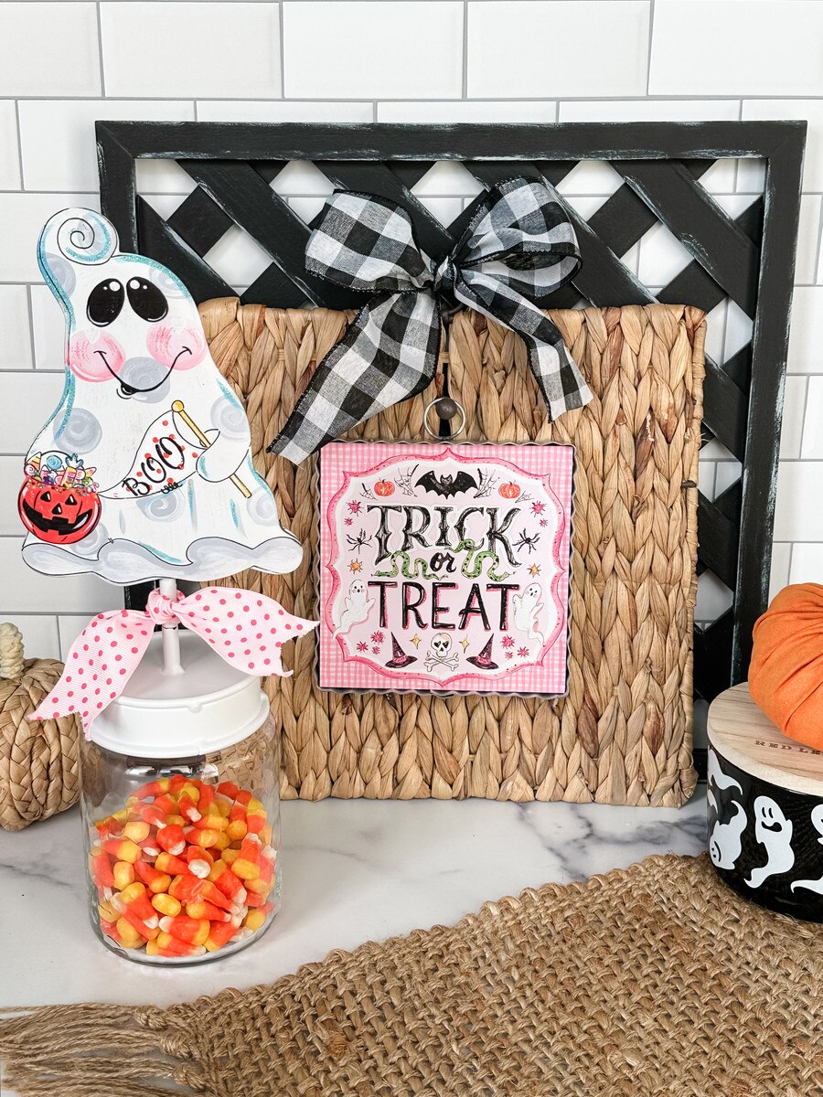 Halloween-themed decor with ghost, candy jar, and 'Trick or Treat' sign on a white tiled wall background.