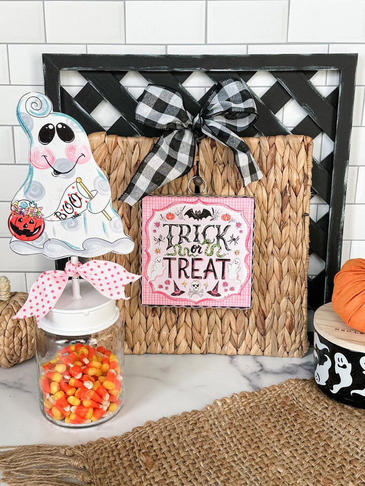 Halloween-themed decor with ghost, candy jar, and 'Trick or Treat' sign on a white tiled wall background.